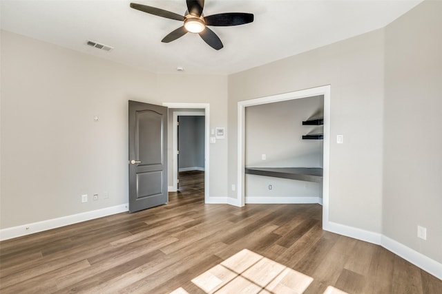 empty room with hardwood / wood-style flooring, built in desk, and ceiling fan