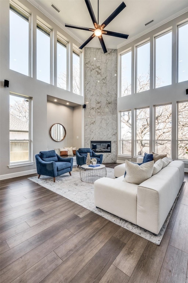 living room with ornamental molding, dark hardwood / wood-style floors, ceiling fan, a tiled fireplace, and a high ceiling