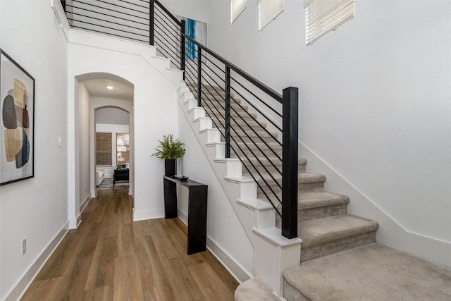 staircase with baseboards, a high ceiling, arched walkways, and wood finished floors