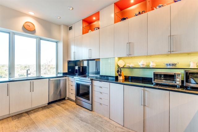 kitchen with appliances with stainless steel finishes, white cabinetry, sink, decorative backsplash, and light hardwood / wood-style floors