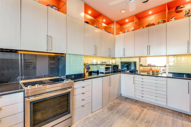 kitchen with white cabinets, decorative backsplash, stainless steel range with electric stovetop, ceiling fan, and light hardwood / wood-style floors