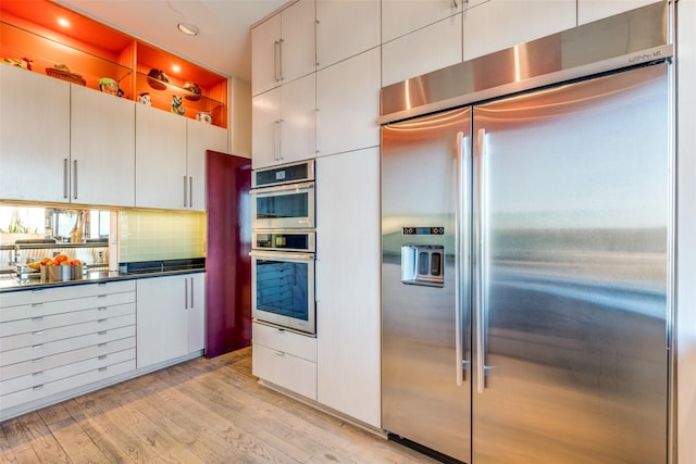 kitchen with white cabinetry, stainless steel appliances, tasteful backsplash, and light wood-type flooring