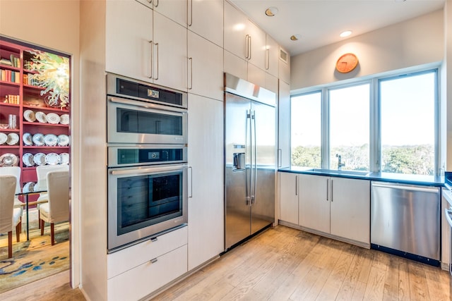 kitchen featuring sink, light hardwood / wood-style floors, white cabinets, and appliances with stainless steel finishes