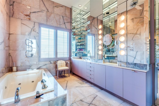 bathroom featuring a relaxing tiled tub, vanity, and tile walls