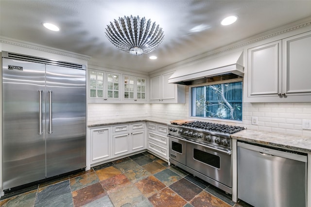 kitchen with premium range hood, tasteful backsplash, white cabinets, high end appliances, and light stone countertops