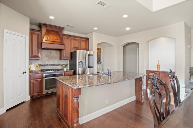 kitchen with premium range hood, sink, a center island with sink, appliances with stainless steel finishes, and backsplash