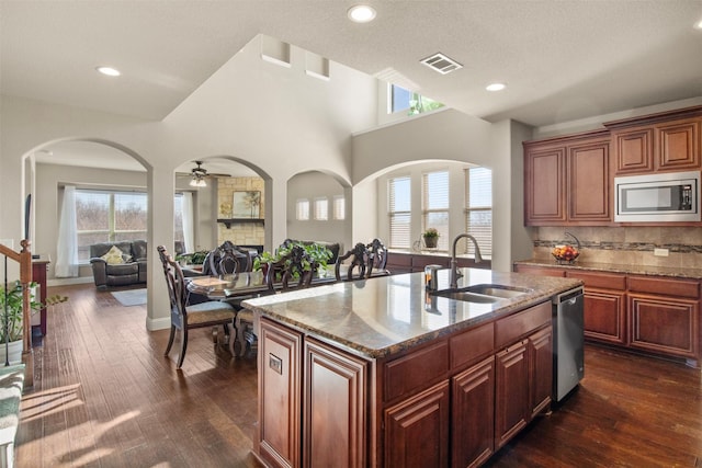 kitchen with stainless steel appliances, stone countertops, sink, and a center island with sink