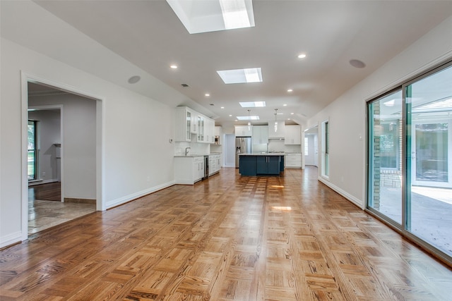 unfurnished living room with light parquet floors, lofted ceiling with skylight, and sink