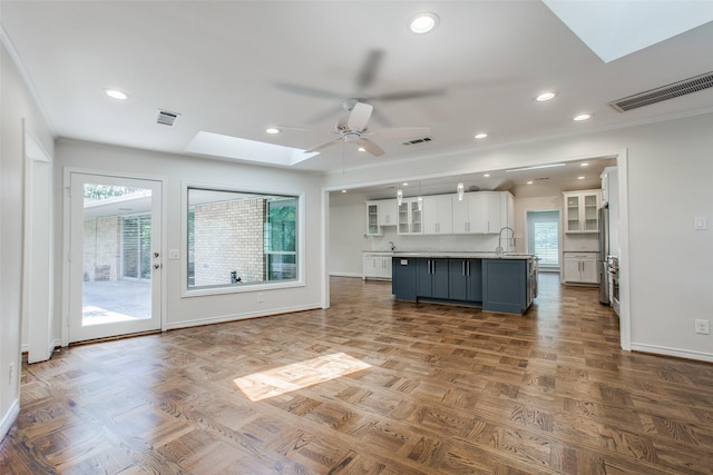 kitchen featuring stainless steel refrigerator, a skylight, white cabinetry, a kitchen island with sink, and ceiling fan