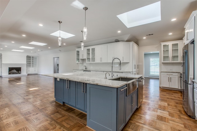 kitchen with hanging light fixtures, white cabinetry, a large island with sink, and a skylight