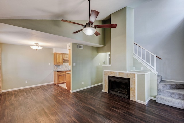 unfurnished living room featuring sink, high vaulted ceiling, dark hardwood / wood-style flooring, a tile fireplace, and ceiling fan