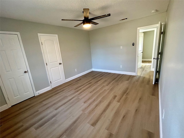 unfurnished bedroom with multiple closets, light wood-type flooring, a textured ceiling, and ceiling fan