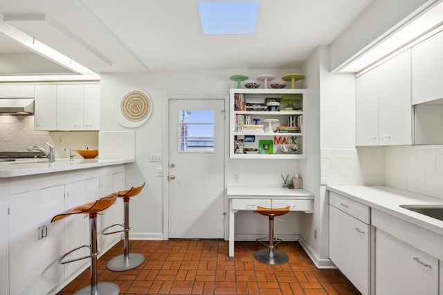 kitchen featuring brick floor, a sink, white cabinetry, and under cabinet range hood