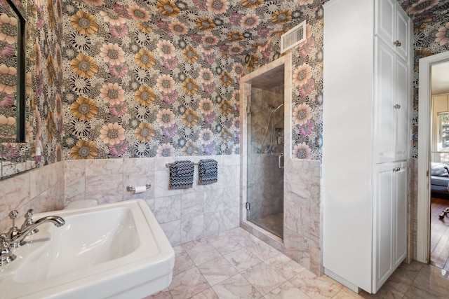 full bathroom with wallpapered walls, a stall shower, visible vents, a sink, and tile walls