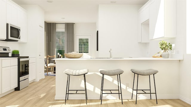 kitchen with a breakfast bar, sink, white cabinets, stainless steel appliances, and light hardwood / wood-style flooring