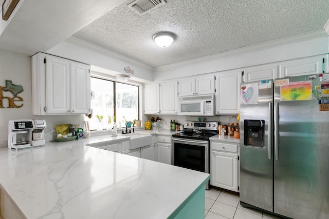 kitchen with sink, light tile patterned floors, appliances with stainless steel finishes, white cabinetry, and a textured ceiling