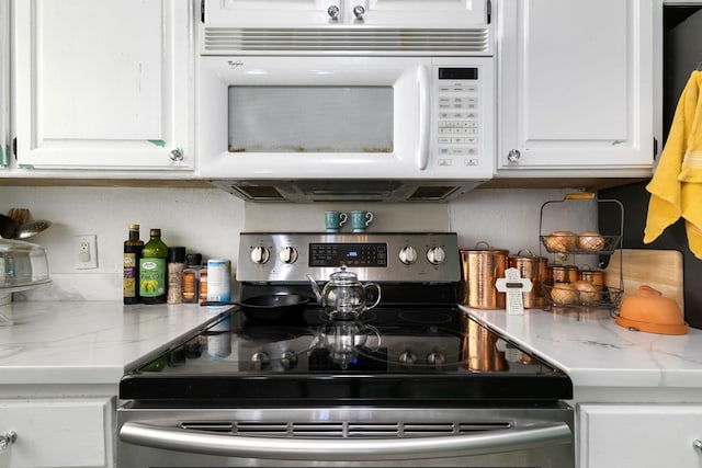 kitchen with electric stove, light stone counters, and white cabinets