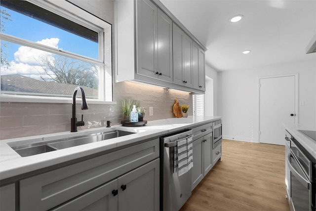 kitchen featuring appliances with stainless steel finishes, a sink, light wood-style flooring, and gray cabinetry