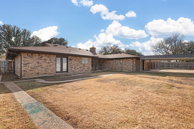 back of property with brick siding, fence, french doors, a lawn, and a chimney