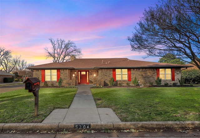 ranch-style home with brick siding, a lawn, and a chimney