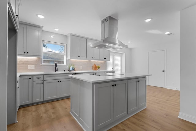 kitchen with a center island, island exhaust hood, black electric stovetop, gray cabinets, and a sink