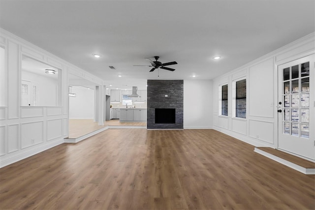 unfurnished living room with wood finished floors, a decorative wall, a stone fireplace, and ceiling fan