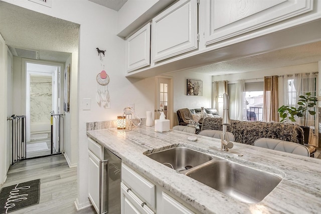 kitchen with white cabinetry, light stone countertops, sink, and light hardwood / wood-style flooring