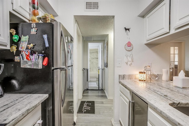 kitchen with white cabinets, stainless steel fridge, and light hardwood / wood-style floors