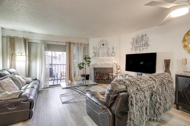 living room with a tile fireplace, a textured ceiling, and light hardwood / wood-style floors