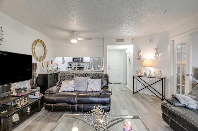 living room featuring ceiling fan, light hardwood / wood-style floors, and a textured ceiling