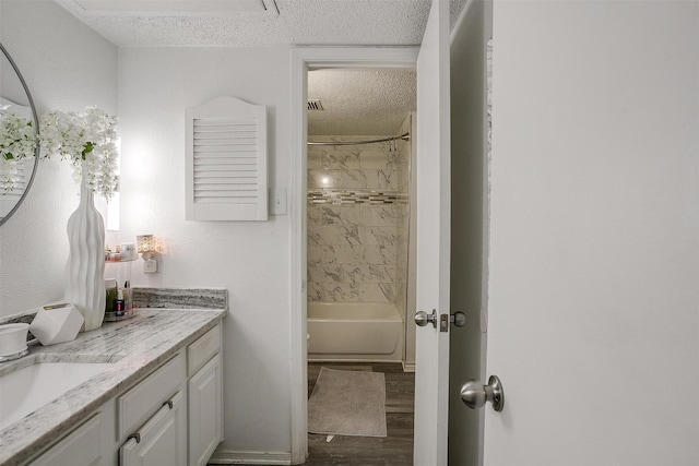 bathroom with vanity, tiled shower / bath, wood-type flooring, and a textured ceiling