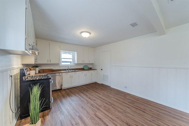 kitchen featuring sink, appliances with stainless steel finishes, white cabinetry, hardwood / wood-style floors, and beamed ceiling