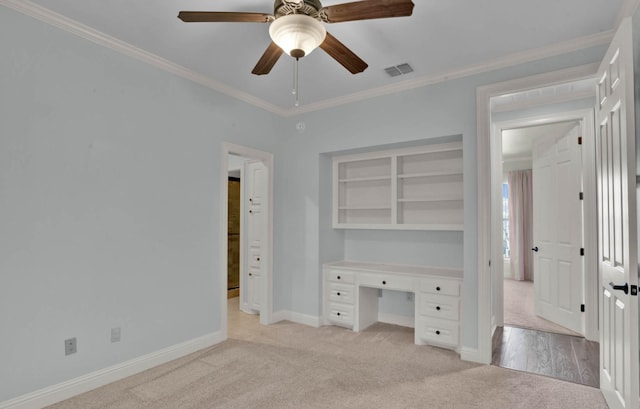 unfurnished office with crown molding, built in desk, ceiling fan, built in features, and light colored carpet