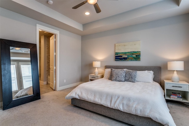 carpeted bedroom featuring a tray ceiling, ensuite bath, and ceiling fan