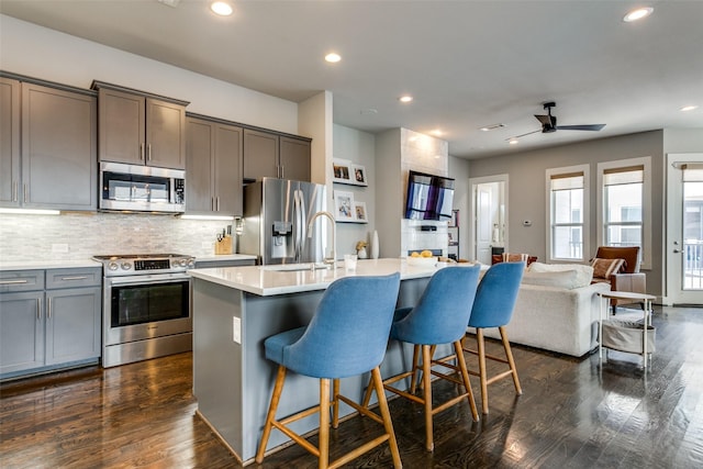 kitchen featuring dark wood-type flooring, a center island with sink, a breakfast bar, and appliances with stainless steel finishes