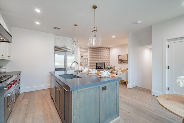 kitchen featuring sink, white cabinetry, high quality appliances, pendant lighting, and a kitchen island with sink