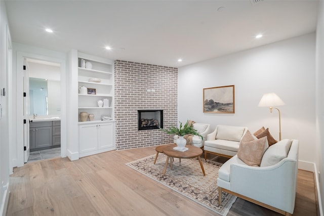 living room featuring built in shelves, a fireplace, and light wood-type flooring