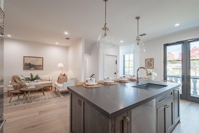 kitchen featuring french doors, sink, light hardwood / wood-style flooring, hanging light fixtures, and a center island with sink