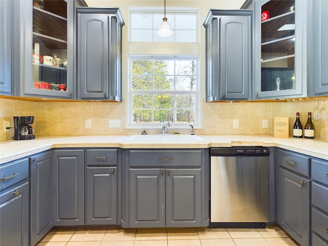 kitchen with tasteful backsplash, dishwasher, sink, hanging light fixtures, and light tile patterned floors