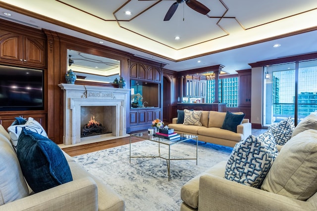 living room with hardwood / wood-style flooring, ornamental molding, ceiling fan, a tray ceiling, and a premium fireplace