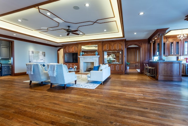 living room with ornamental molding, dark hardwood / wood-style floors, a raised ceiling, and ceiling fan with notable chandelier