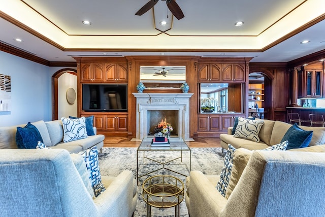 living room featuring ornamental molding, a raised ceiling, ceiling fan, and light wood-type flooring