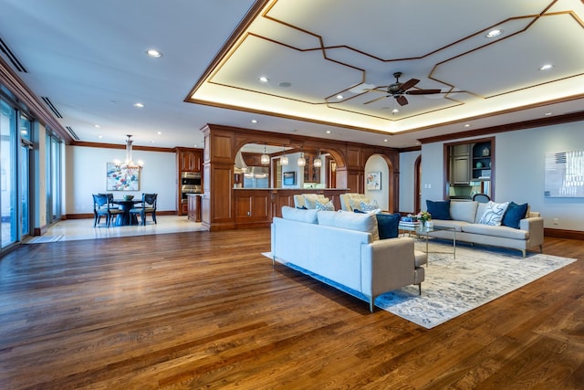 living room featuring dark hardwood / wood-style flooring, a tray ceiling, ceiling fan with notable chandelier, and crown molding