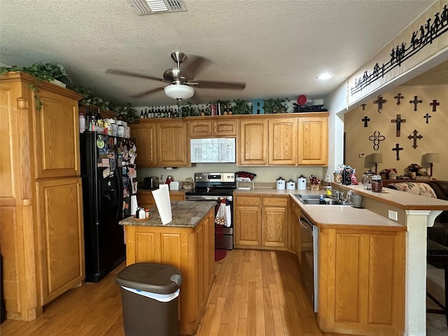 kitchen featuring a breakfast bar area, a center island, a textured ceiling, light hardwood / wood-style flooring, and appliances with stainless steel finishes