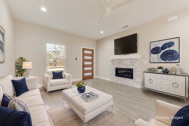 living room featuring ceiling fan, a tiled fireplace, and light hardwood / wood-style floors