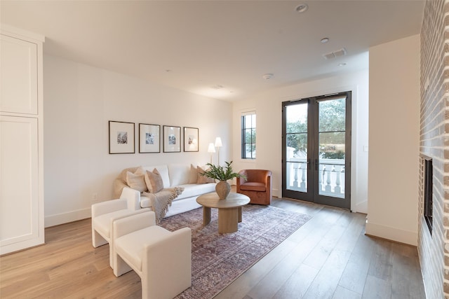 living room with a brick fireplace, light hardwood / wood-style floors, and french doors