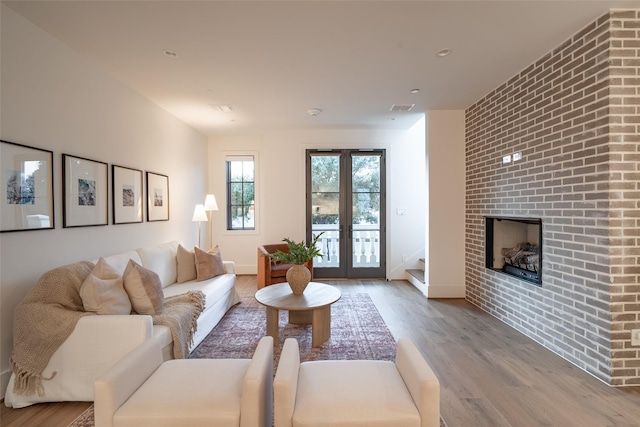 living room featuring a large fireplace, light hardwood / wood-style floors, and french doors