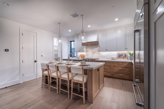 kitchen featuring a breakfast bar area, premium range hood, hanging light fixtures, stainless steel appliances, and a center island with sink