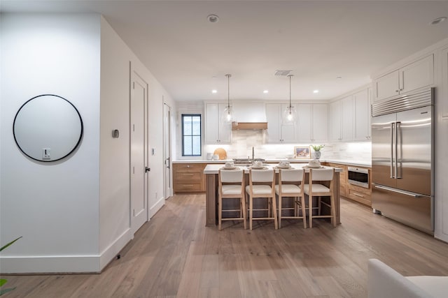 kitchen featuring decorative light fixtures, a center island with sink, stainless steel built in fridge, hardwood / wood-style flooring, and white cabinets