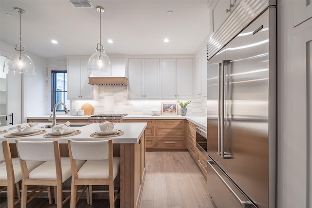 kitchen featuring sink, white cabinetry, stainless steel appliances, decorative light fixtures, and light wood-type flooring